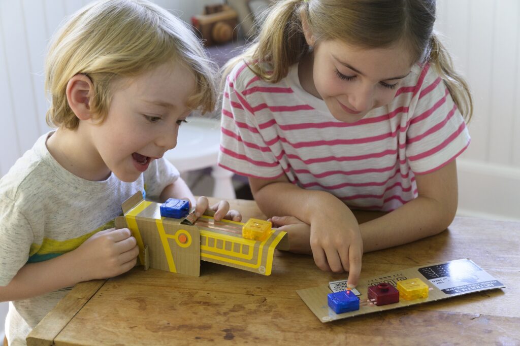 2 happy kids playing with the finished product from our 4M TechCraft Paper Circuit Science